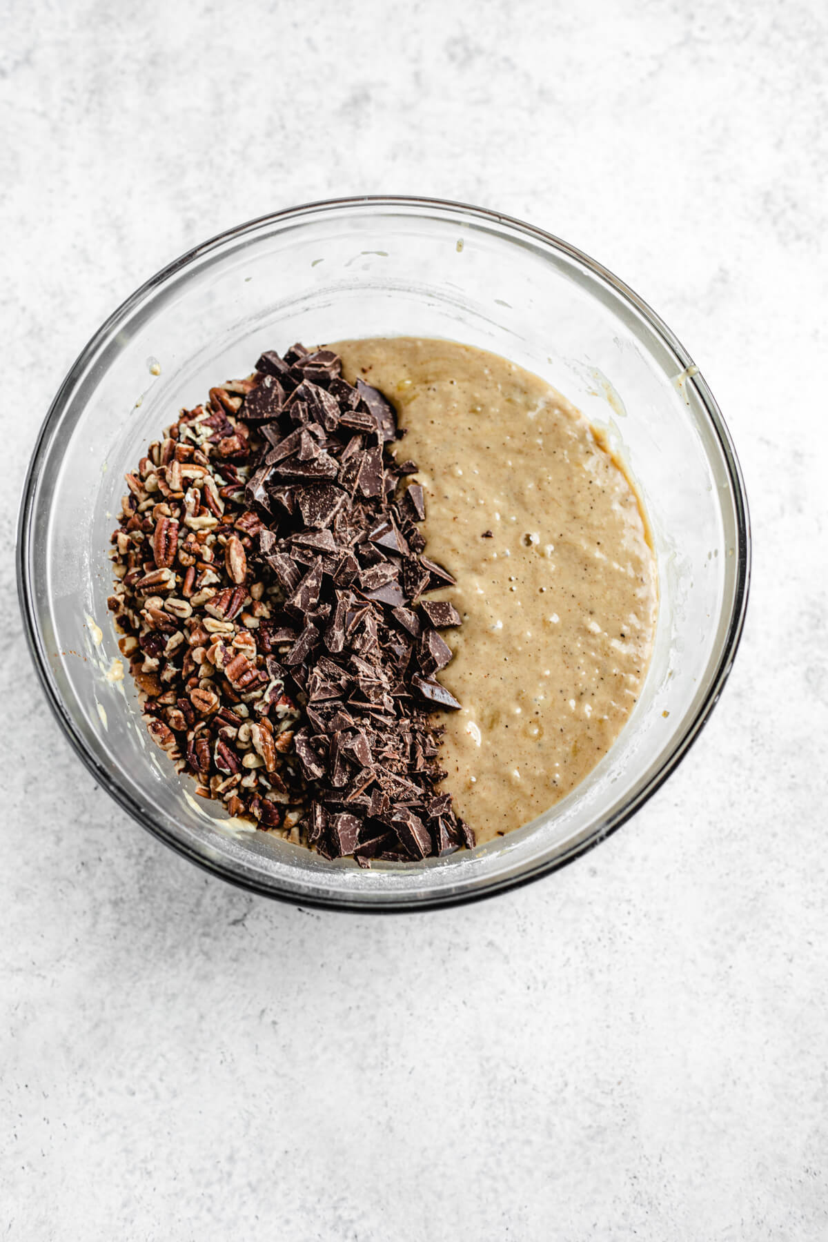 chopped pecans and chopped dark chocolate lined up in a bowl of banana bread batter