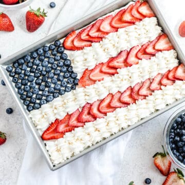 cheesecake decorated with whipped cream, sliced strawberries and blueberries to look like the American flag