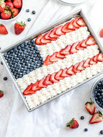 cheesecake decorated with whipped cream, sliced strawberries and blueberries to look like the American flag