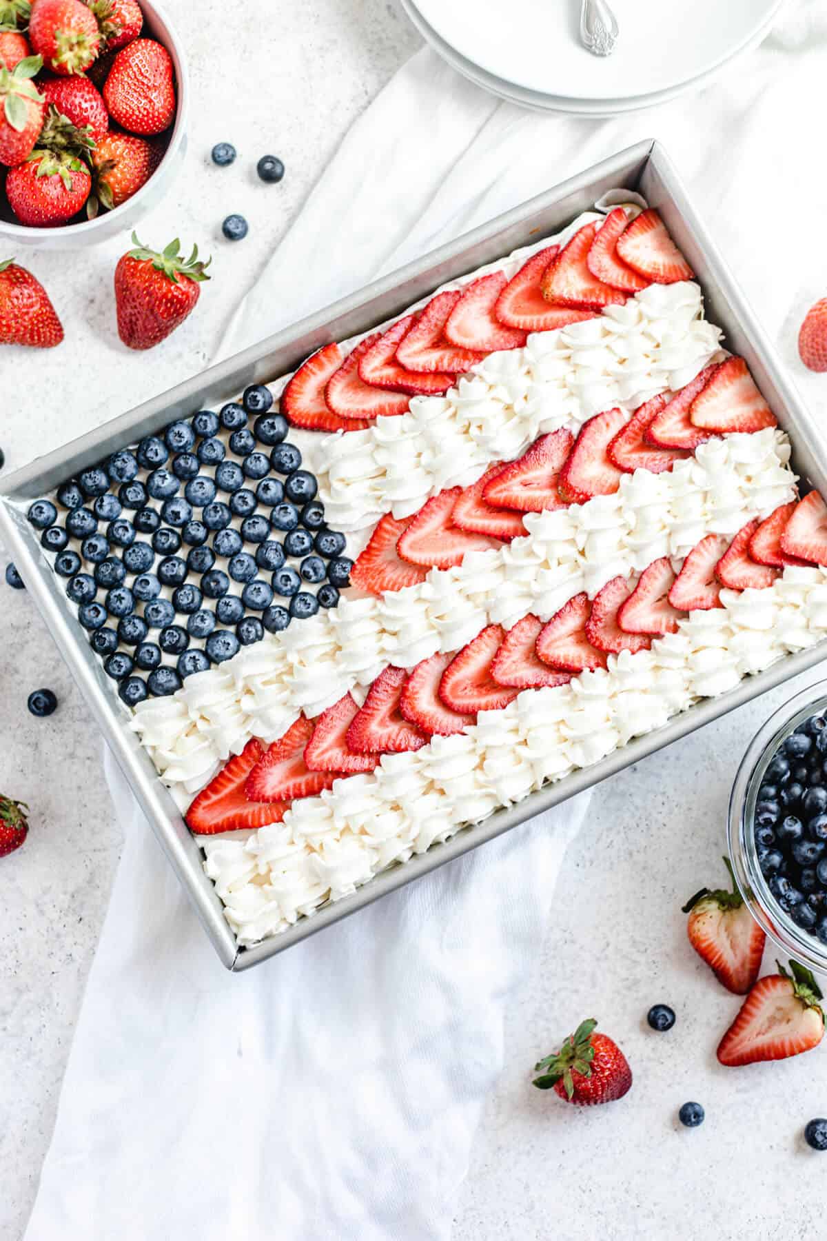 cheesecake decorated with whipped cream, sliced strawberries and blueberries to look like the American flag