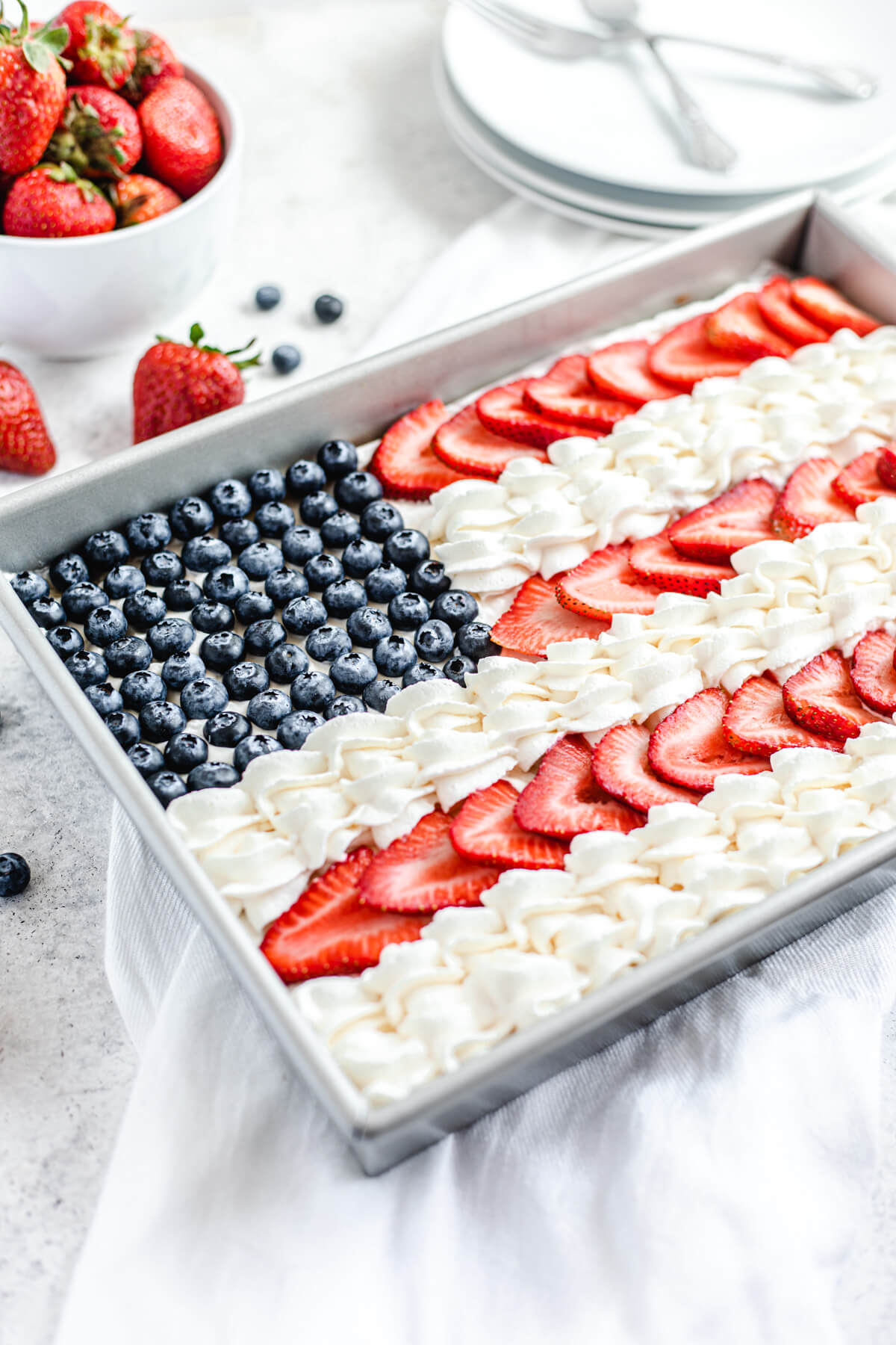 close up angled view of cheesecake in a pan with blueberries, strawberries and whipped cream on top