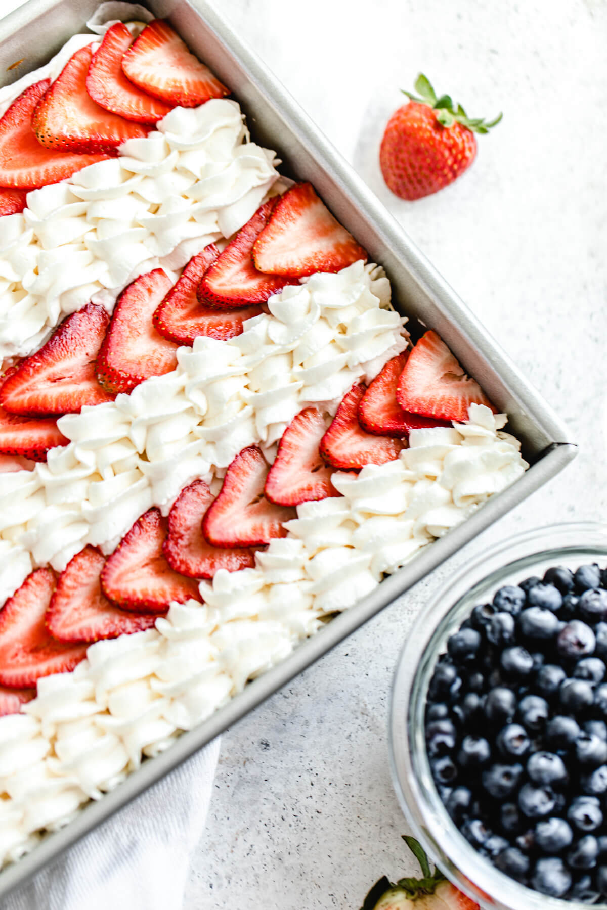 close up of sliced strawberries and whipped cream stripes on a cheesecake