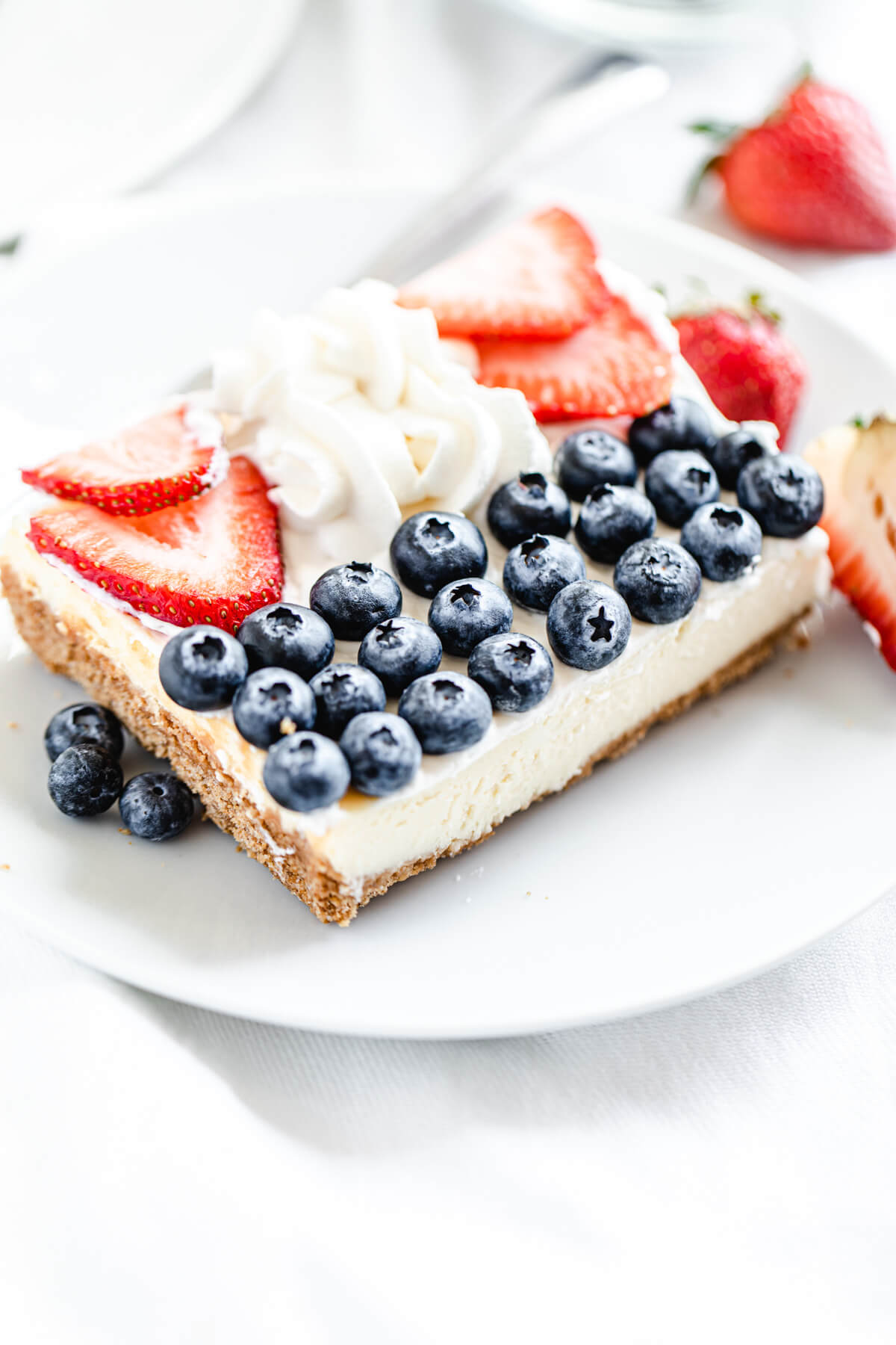 slice of cheesecake with blueberries, whipped cream and strawberries on top on a white plate