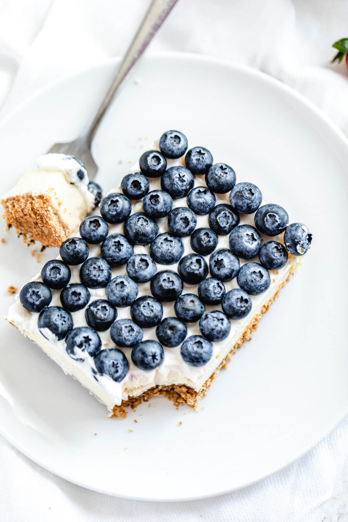 slice of cheesecake with blueberries on top on a white plate with forkful taken out