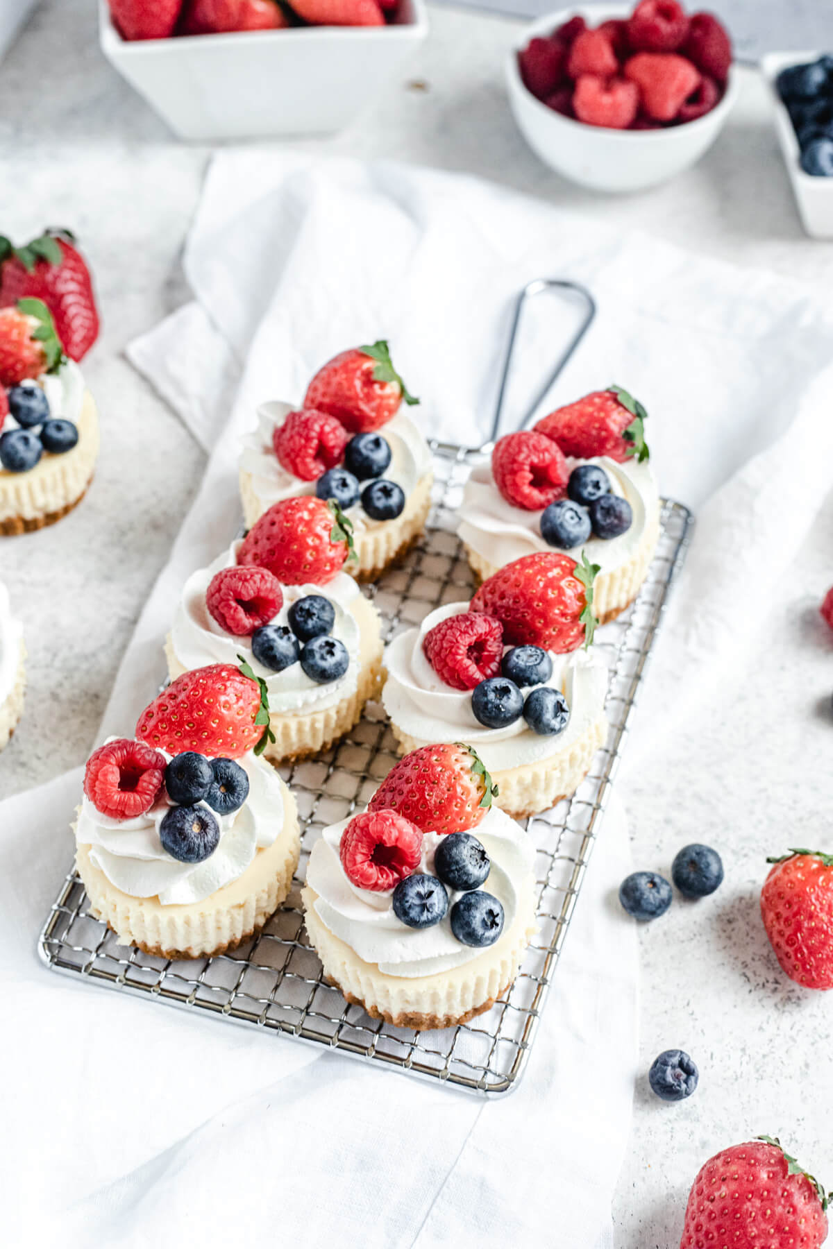 cupcake sized cheesecakes on a safety grater with fresh berries in bowls surrounding them