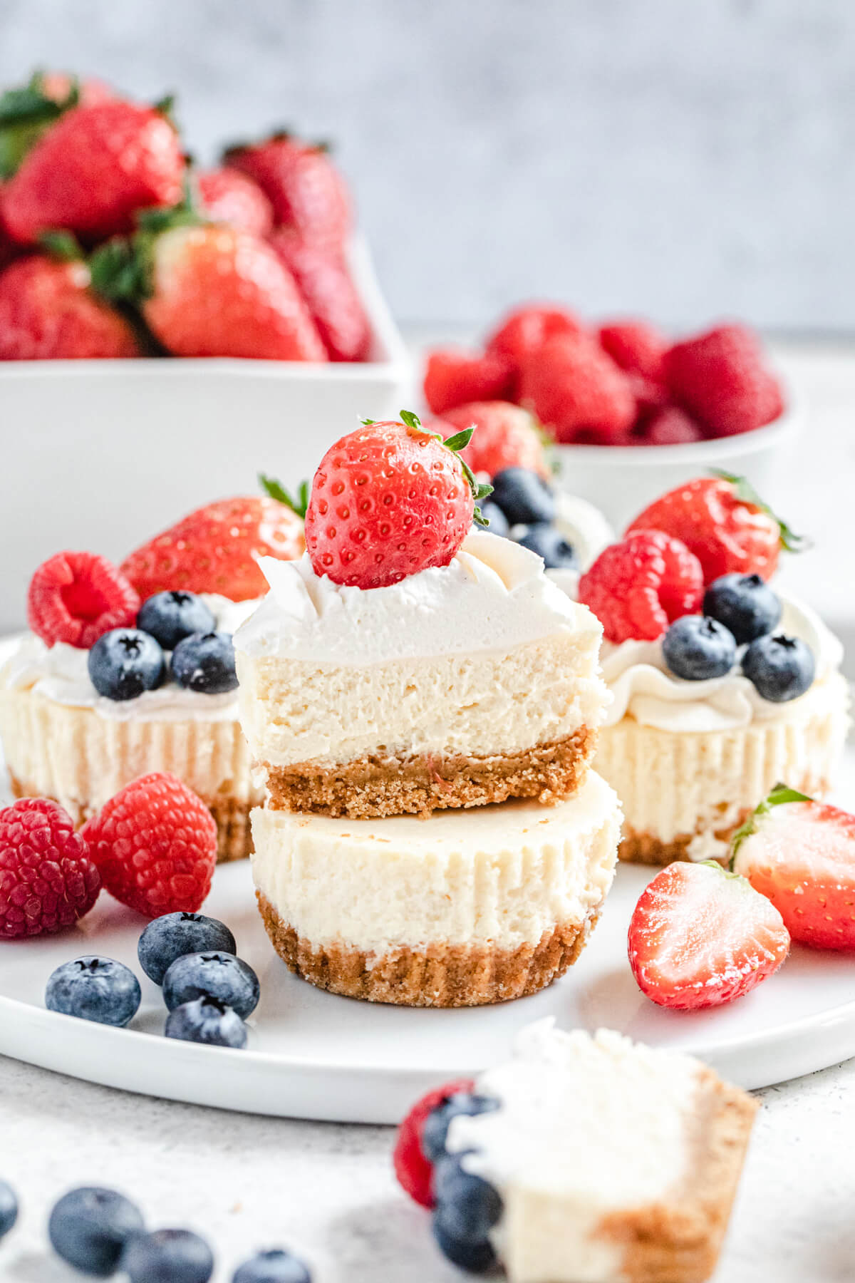 halved mini cheesecake sitting on top of a whole one on a white plate with fresh berries on it