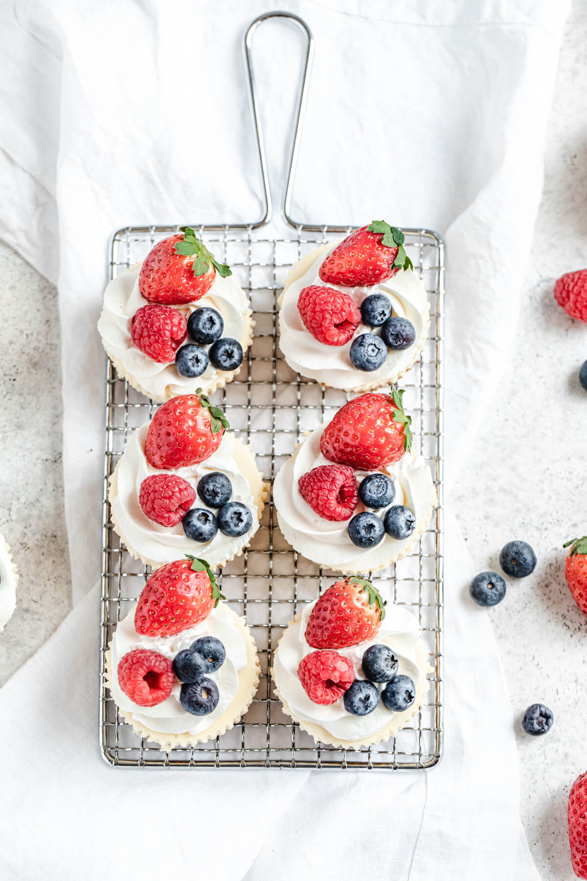 top view of six berry and cream topped cheesecakes on a safety grater