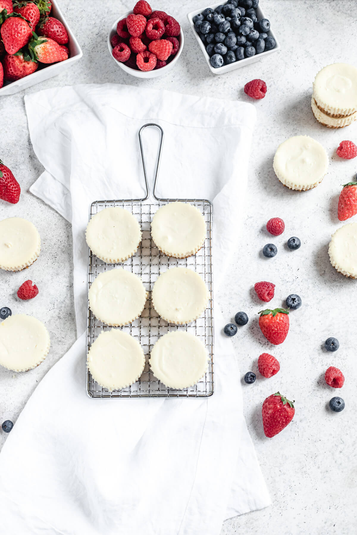 flat-lay view of plain cheesecakes on a safety grater with extras around it and fresh berries in a bowl and scattered around the cheesecakes