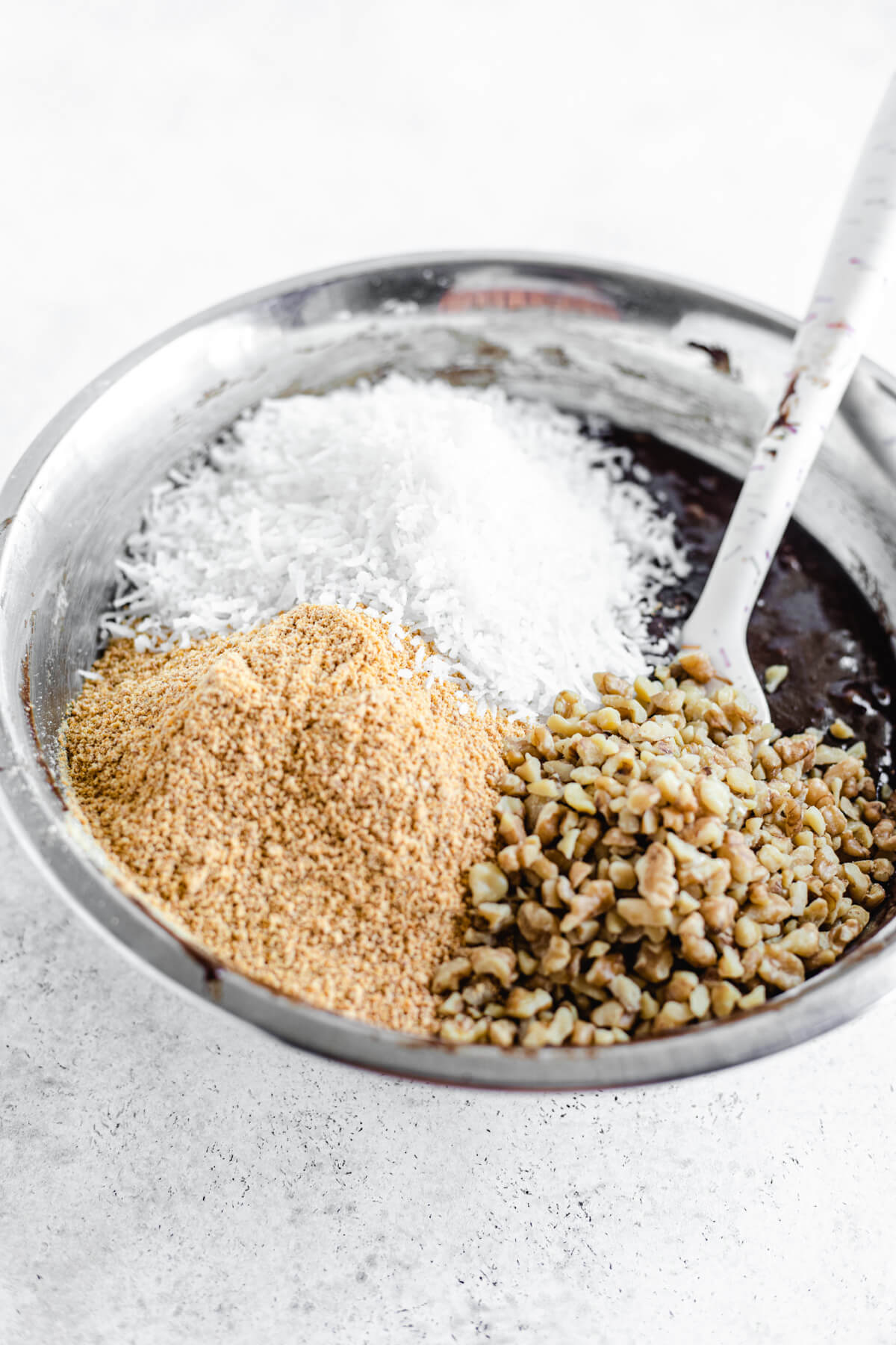 bowl of brownie batter with shredded coconut, graham cracker crumbs and chopped walnuts on top