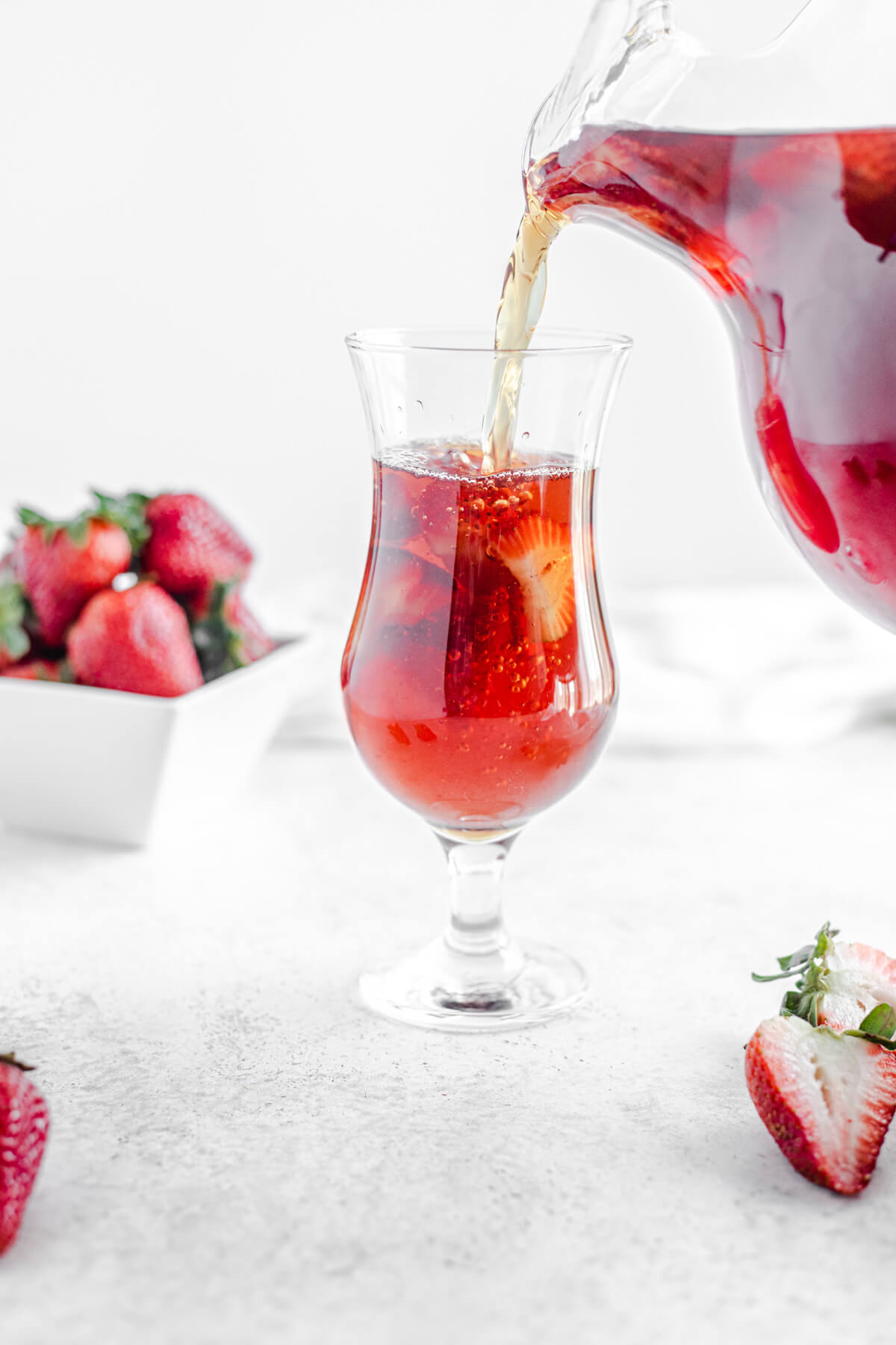 pouring strawberry flavoured iced tea into a glass filled with fresh sliced strawberries