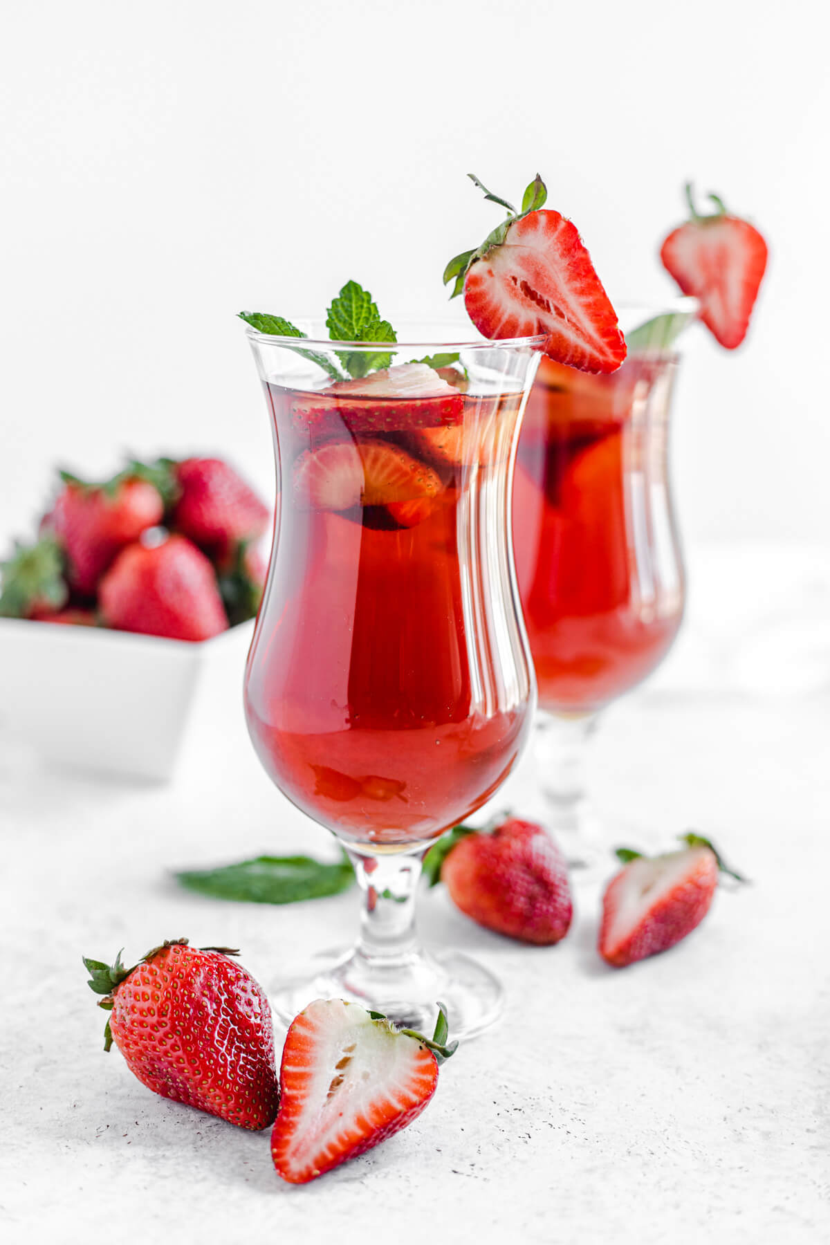 two glasses of iced tea with fresh mint and strawberries inside