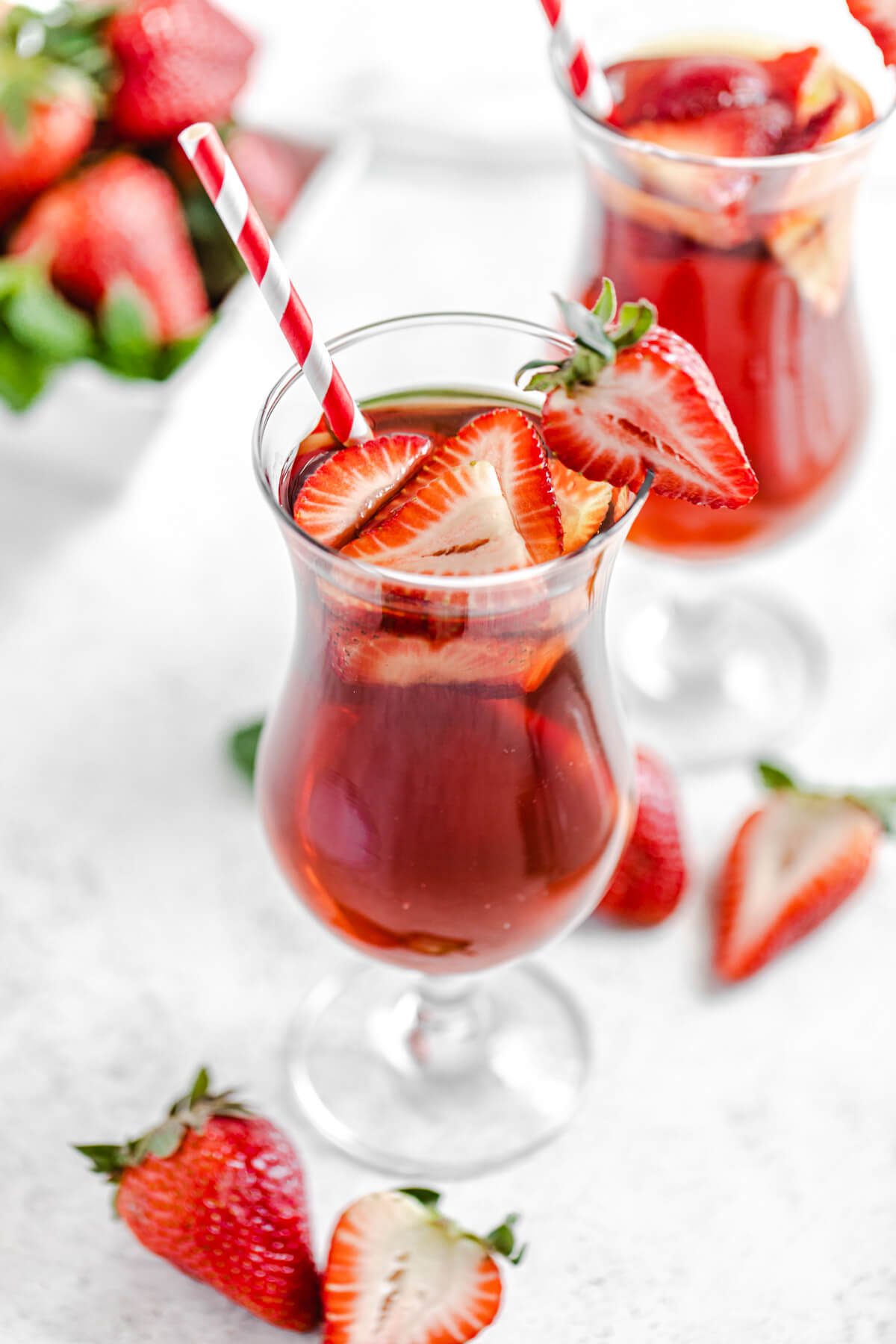 top angled view to show inside of glass with iced tea, fresh strawberries and a red striped paper straw inside