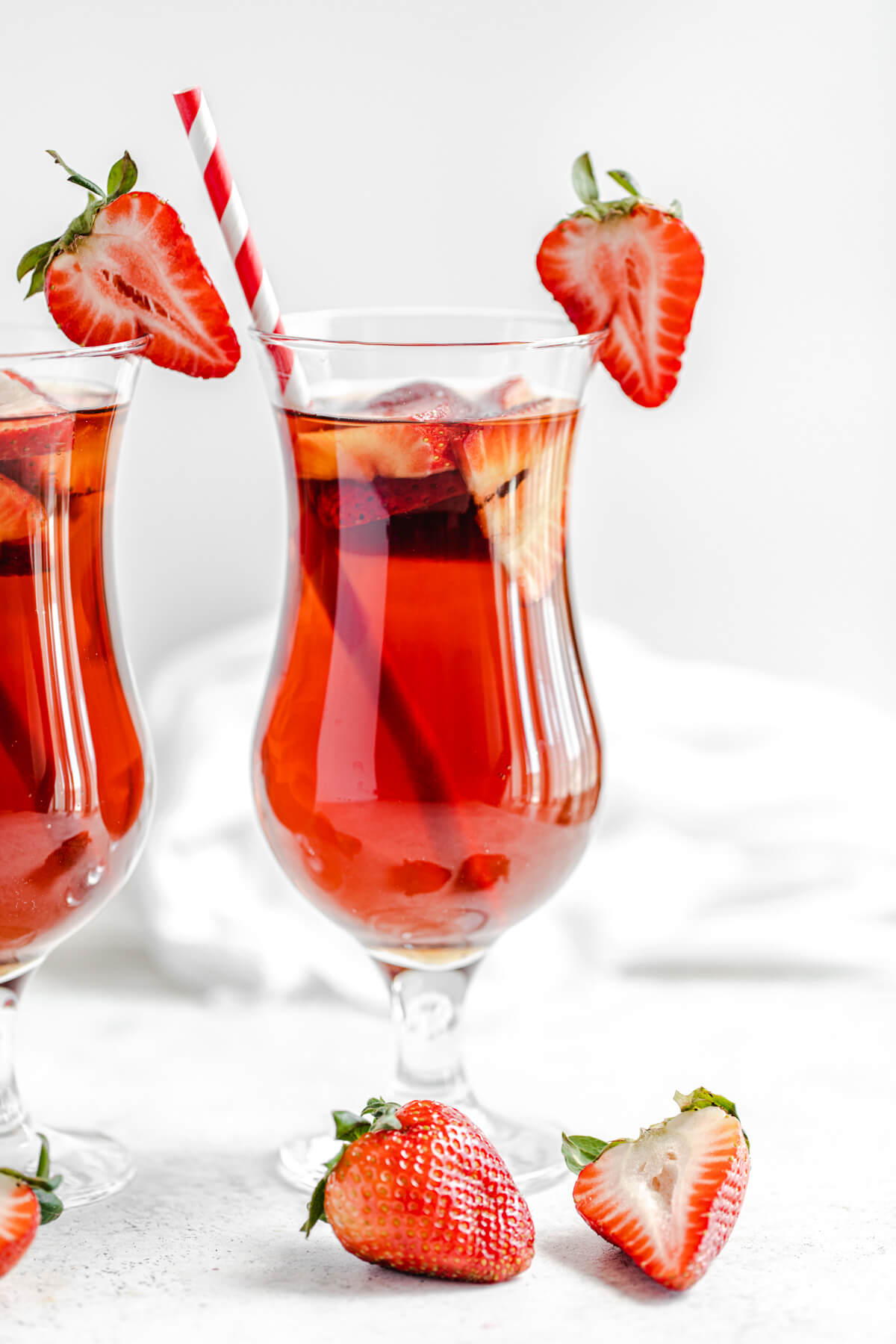 close up of glass of iced tea with halved strawberry on the rim of the glass and a red striped paper straw inside