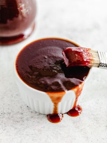 ramekin filled with barbecue sauce dripping over the sides and a dipped pastry brush leaning on the edge