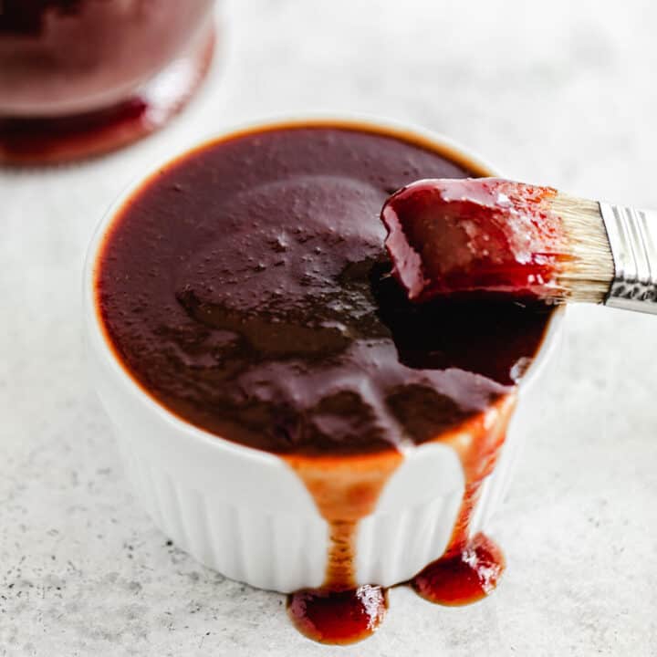 ramekin filled with barbecue sauce dripping over the sides and a dipped pastry brush leaning on the edge