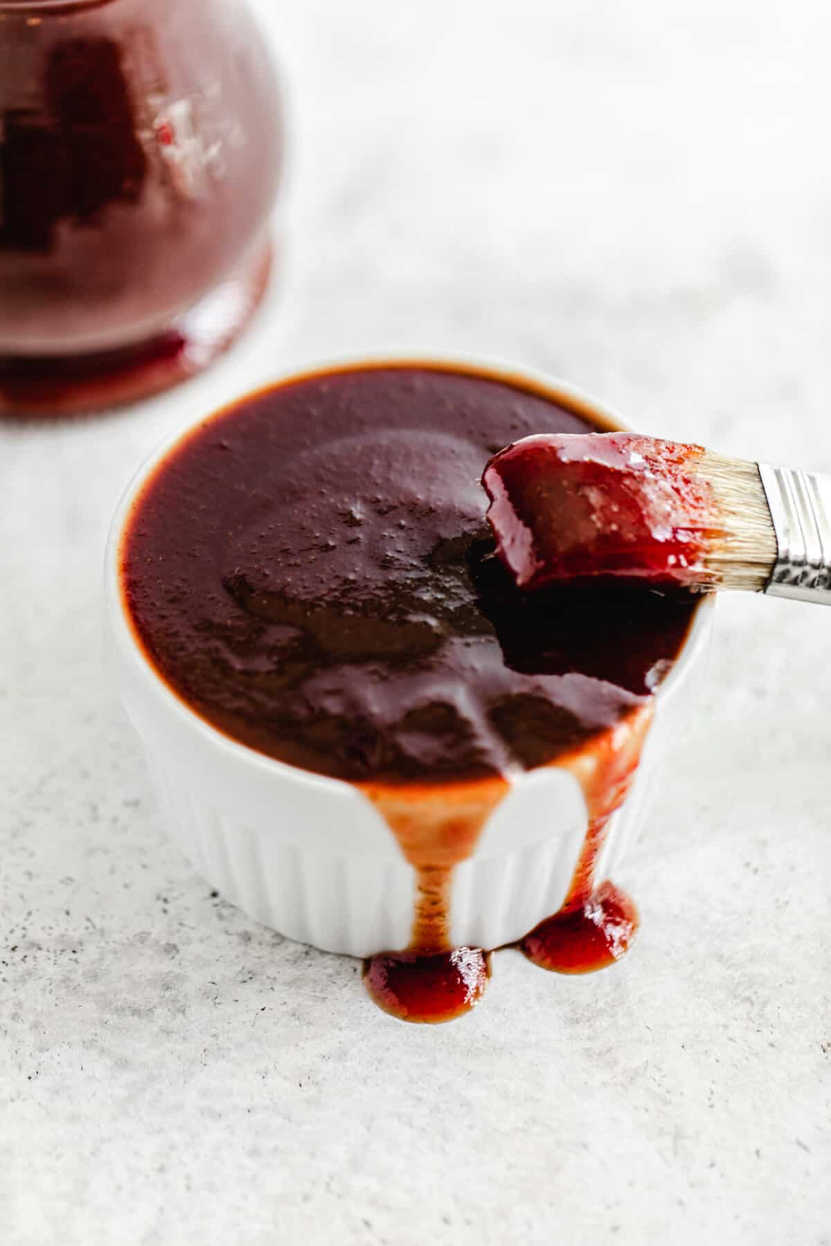 ramekin filled with barbecue sauce dripping over the sides and a dipped pastry brush leaning on the edge