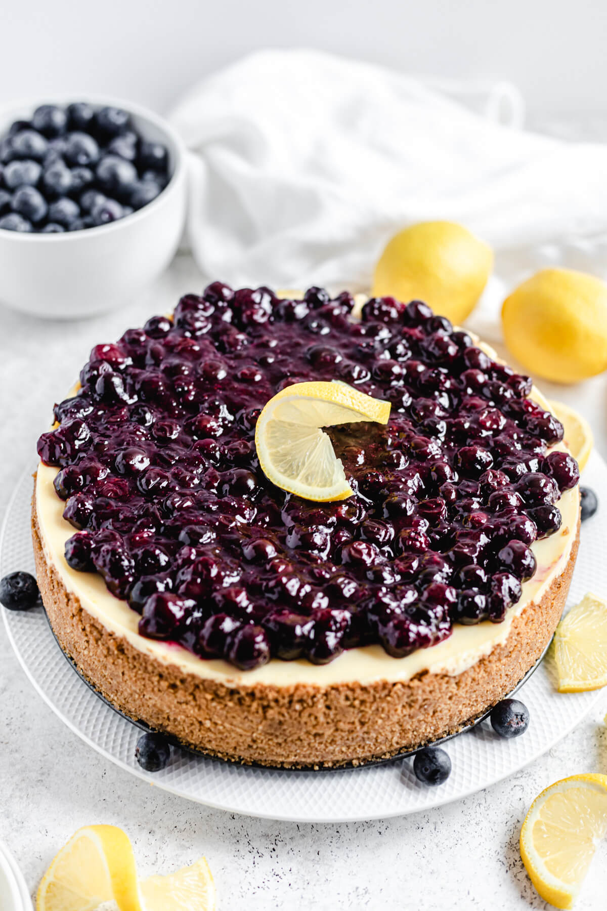 cheesecake on a large white plate with lemons and blueberries around and on top of it