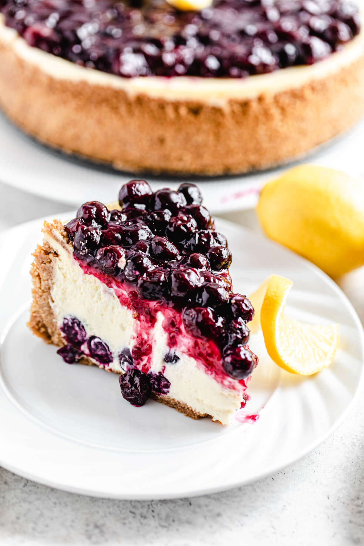 slice of cheesecake on a white plate with whole cheesecake in the background