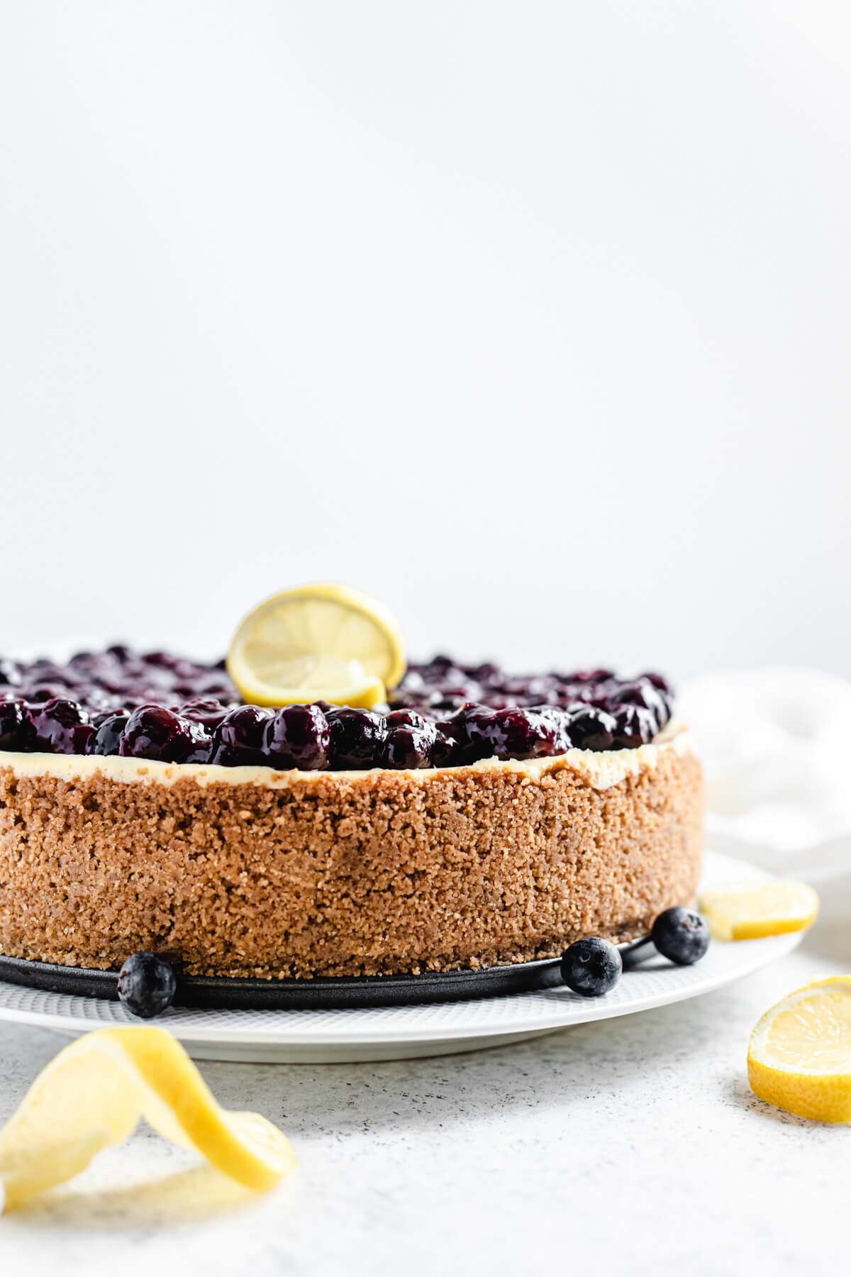 blueberry sauce topped cheesecake on a white plate with fresh blueberries and lemon slices in front of it