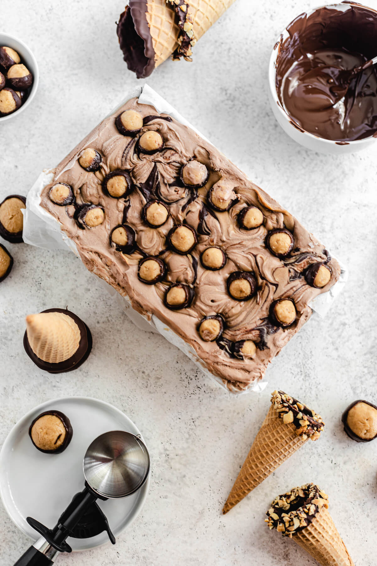 ice cream in a loaf pan with melted chocolate in a bowl, cones and buckeye truffles around it