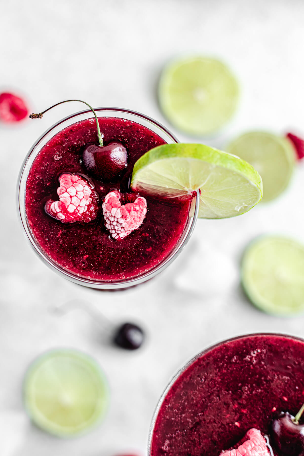 top view showing daiquiri inside of glass topped with two frozen raspberries, a cherry and a lime slice