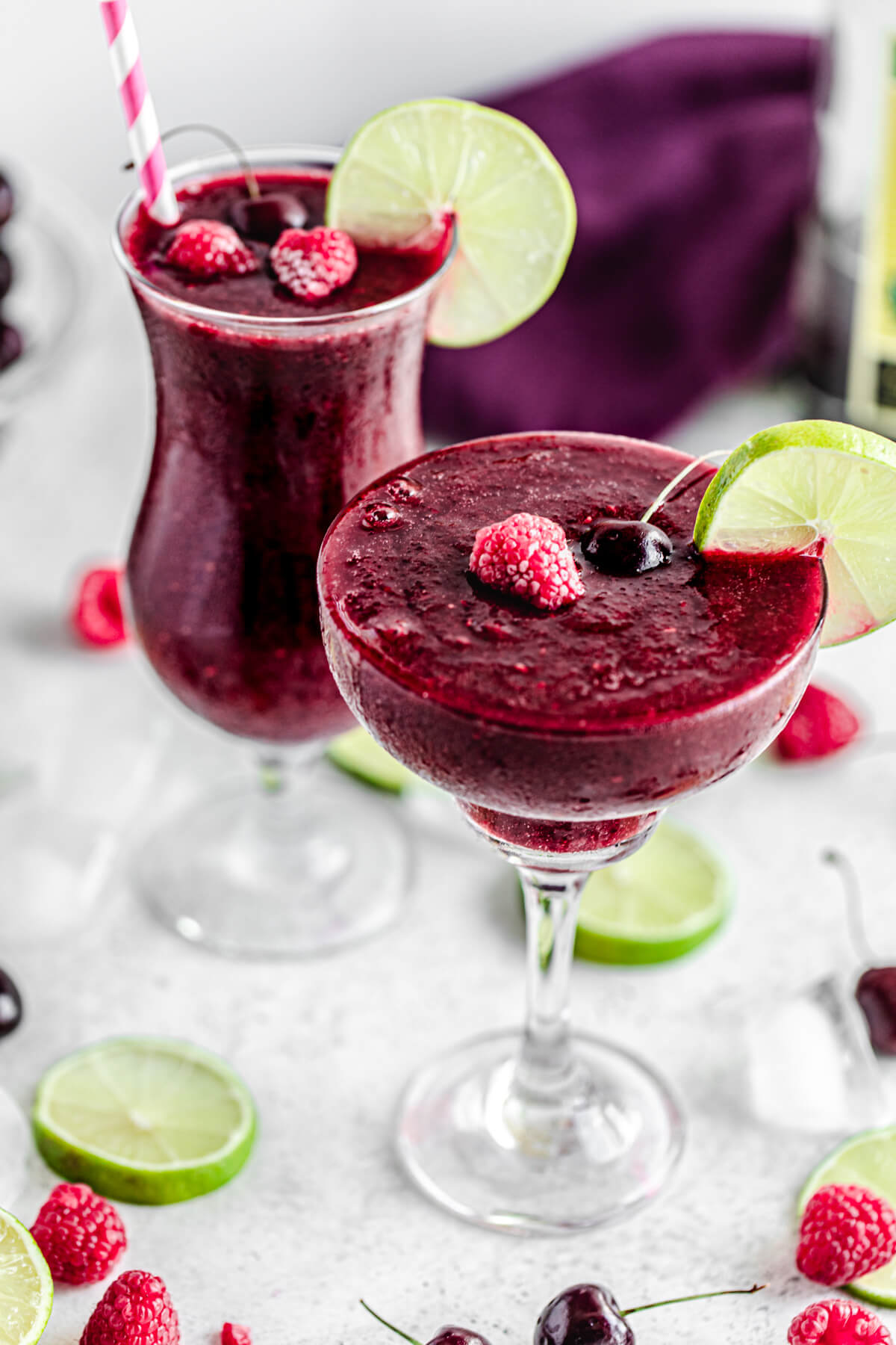 two glasses of cherry daiquiris topped with lime, raspberries and cherries