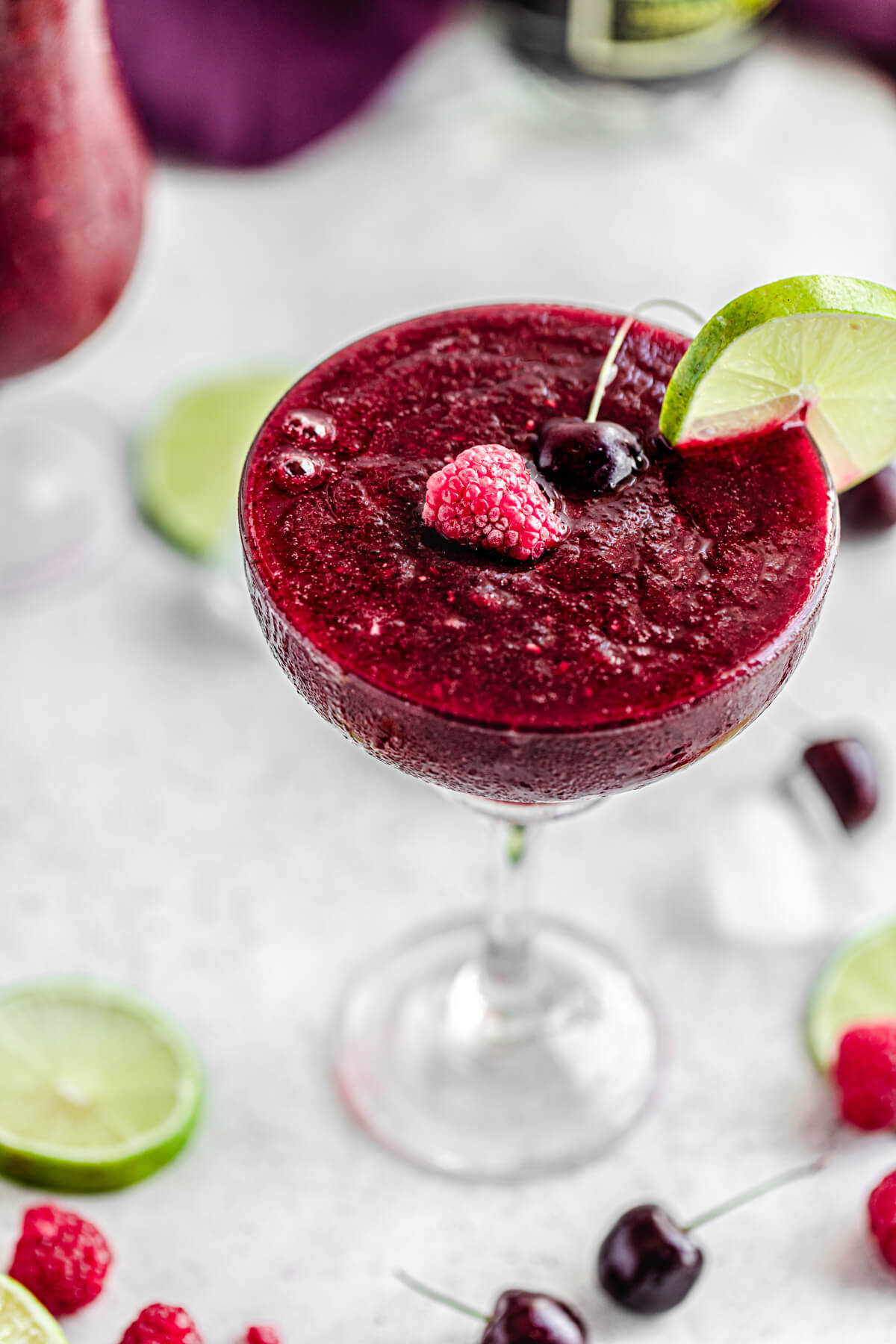 close up of daiquiri in glass topped with frozen raspberries, cherries and lime