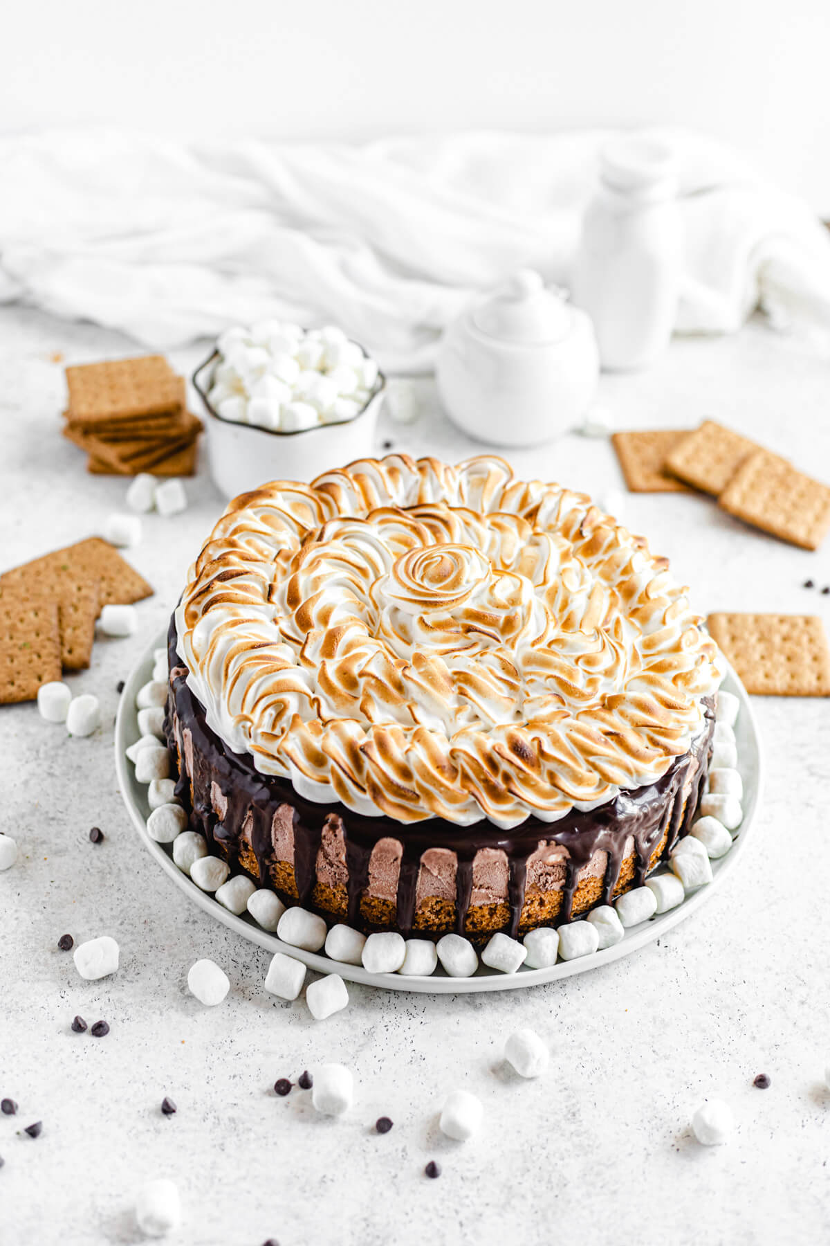 ice cream cake on a white round plate with mini marshmallows and graham cracker squares around it