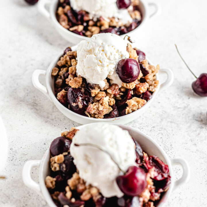 three small plates of cherry crumble topped with a scoop of vanilla ice cream