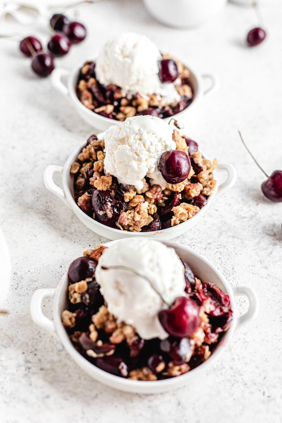 three small plates of cherry crumble topped with a scoop of vanilla ice cream