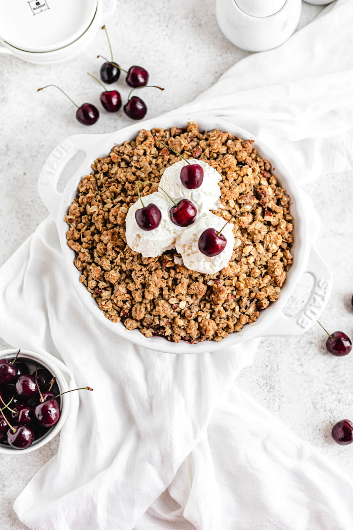 crumble topped with three scoops of vanilla ice cream with fresh cherries on each scoop and in the middle