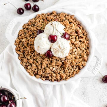 cherry crumble topped with three scoops of vanilla ice cream and fresh cherries