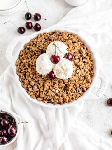cherry crumble topped with three scoops of vanilla ice cream and fresh cherries