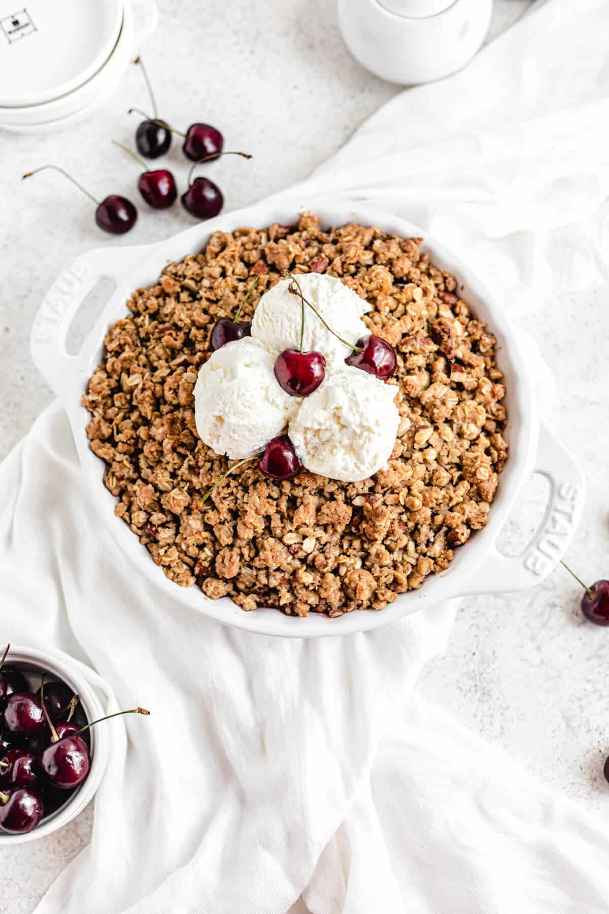 cherry crumble topped with three scoops of vanilla ice cream and fresh cherries