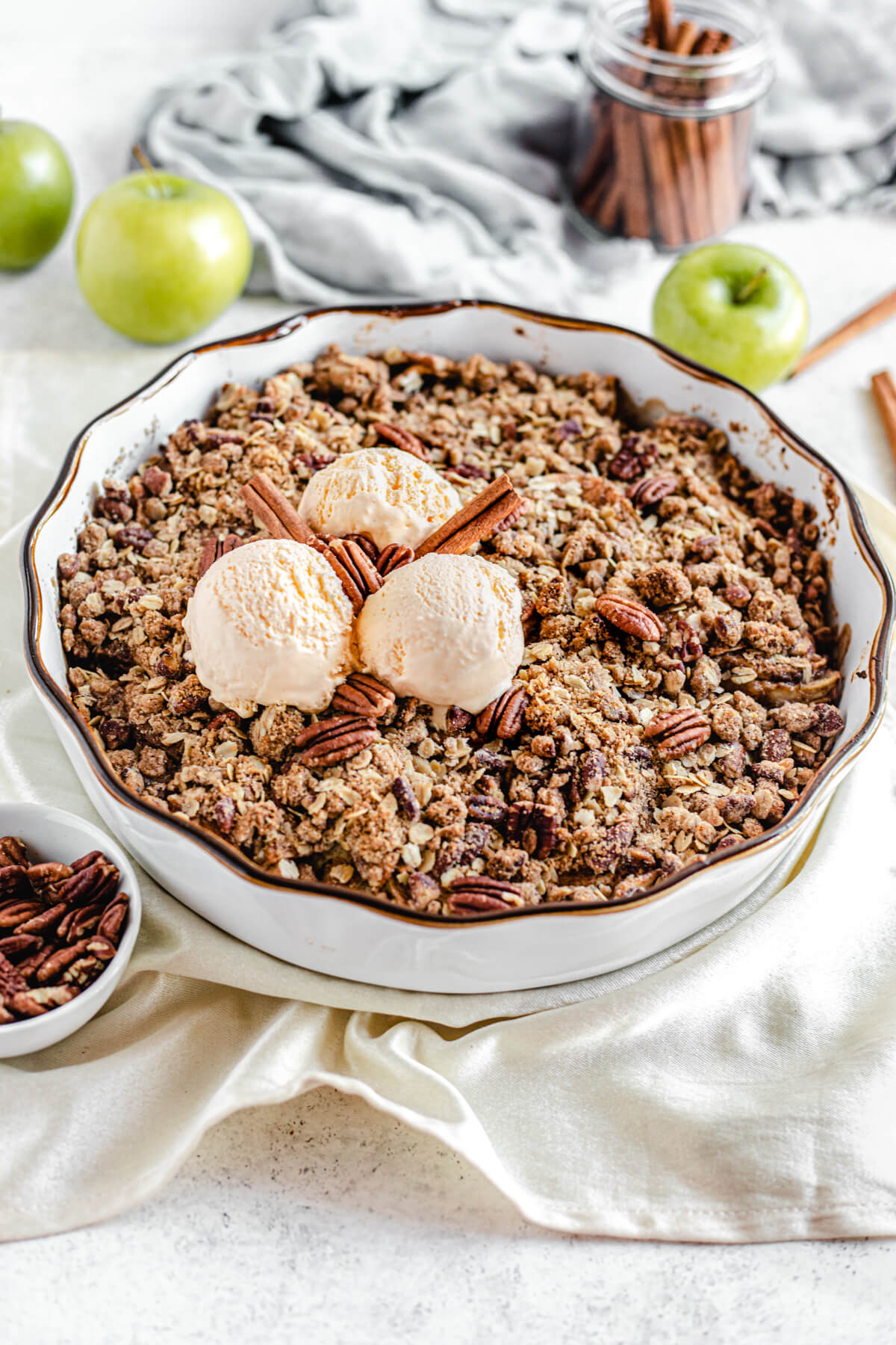 apple crisp in white pie dish topped with ice cream and cinnamon sticks