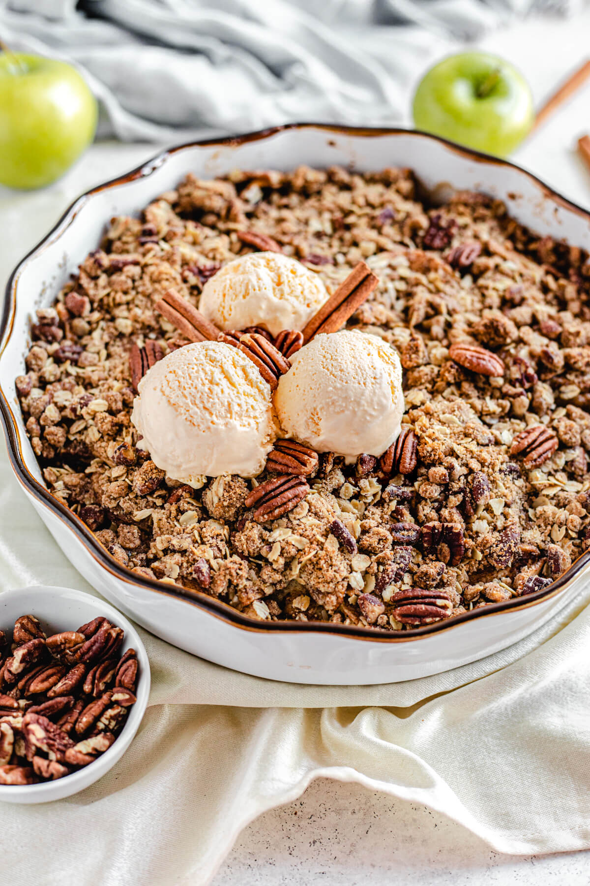 close up of baked apple crisp topped with three scoops of vanilla ice cream and cinnamon sticks