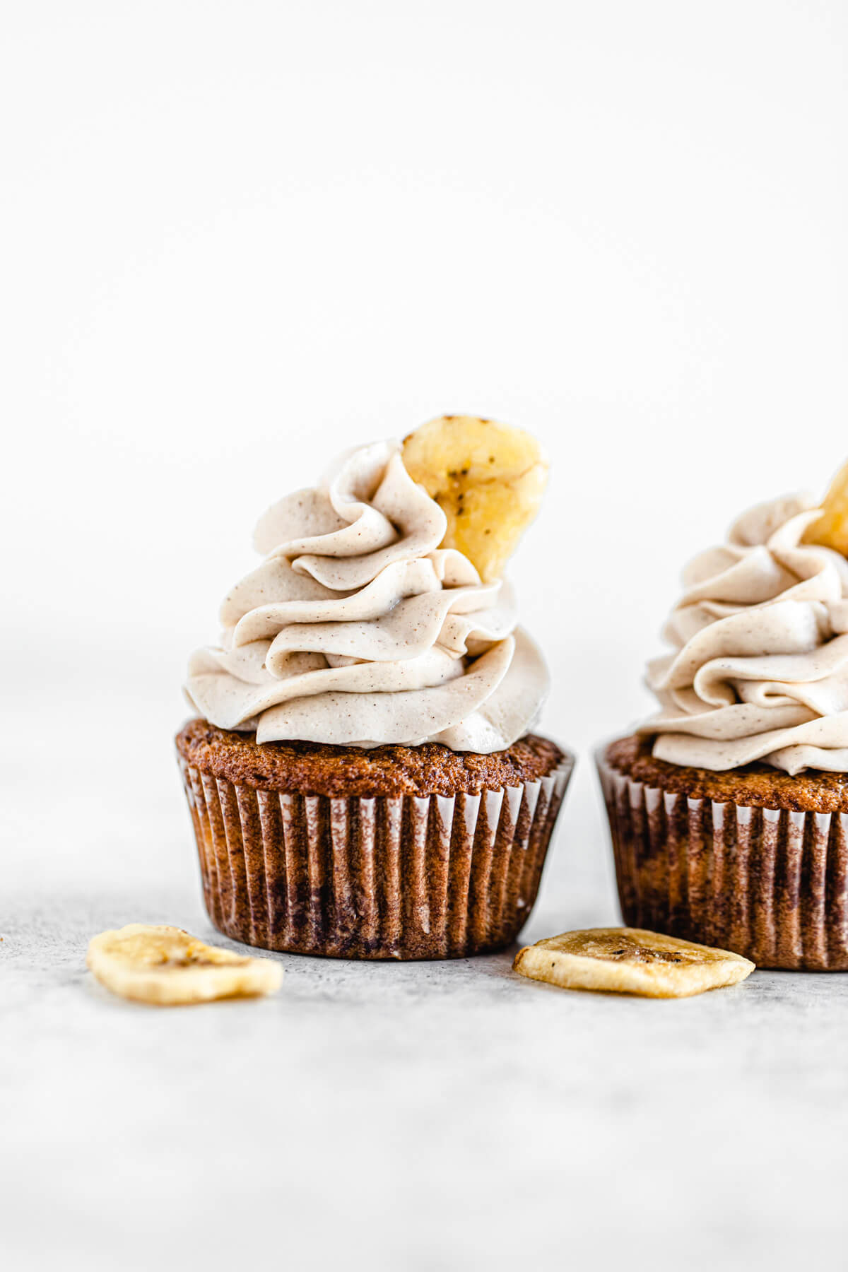 two banana cupcakes side by side with two banana chips beside them