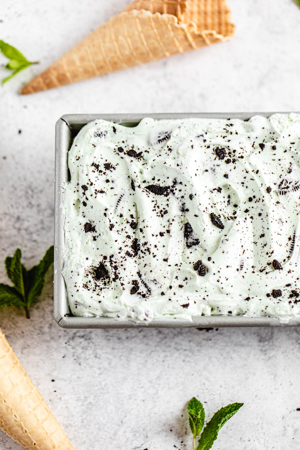 ice cream in a loaf pan with mint leaves and waffle cones around it