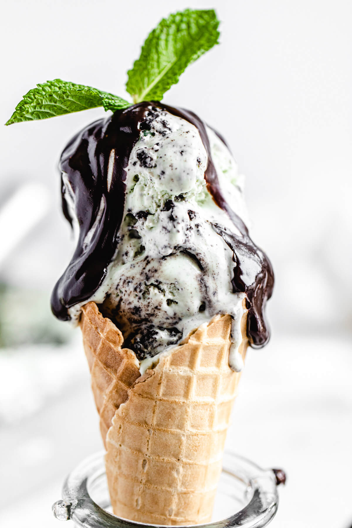 ice cream in a cone topped with ganache and mint leaves