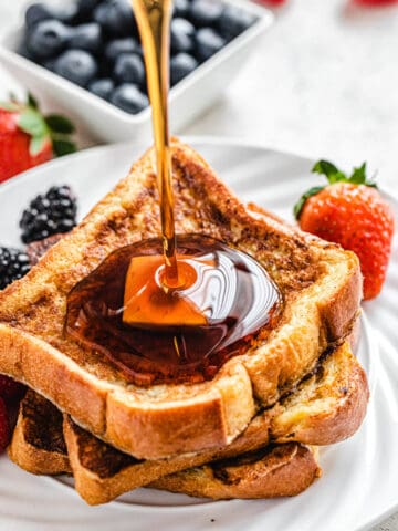 pouring maple syrup onto French toast on a white plate