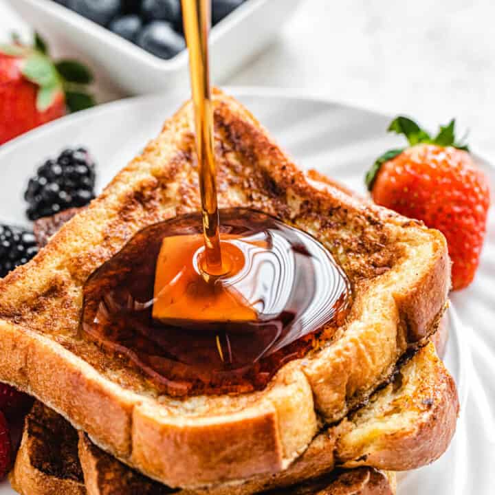 pouring maple syrup onto French toast on a white plate