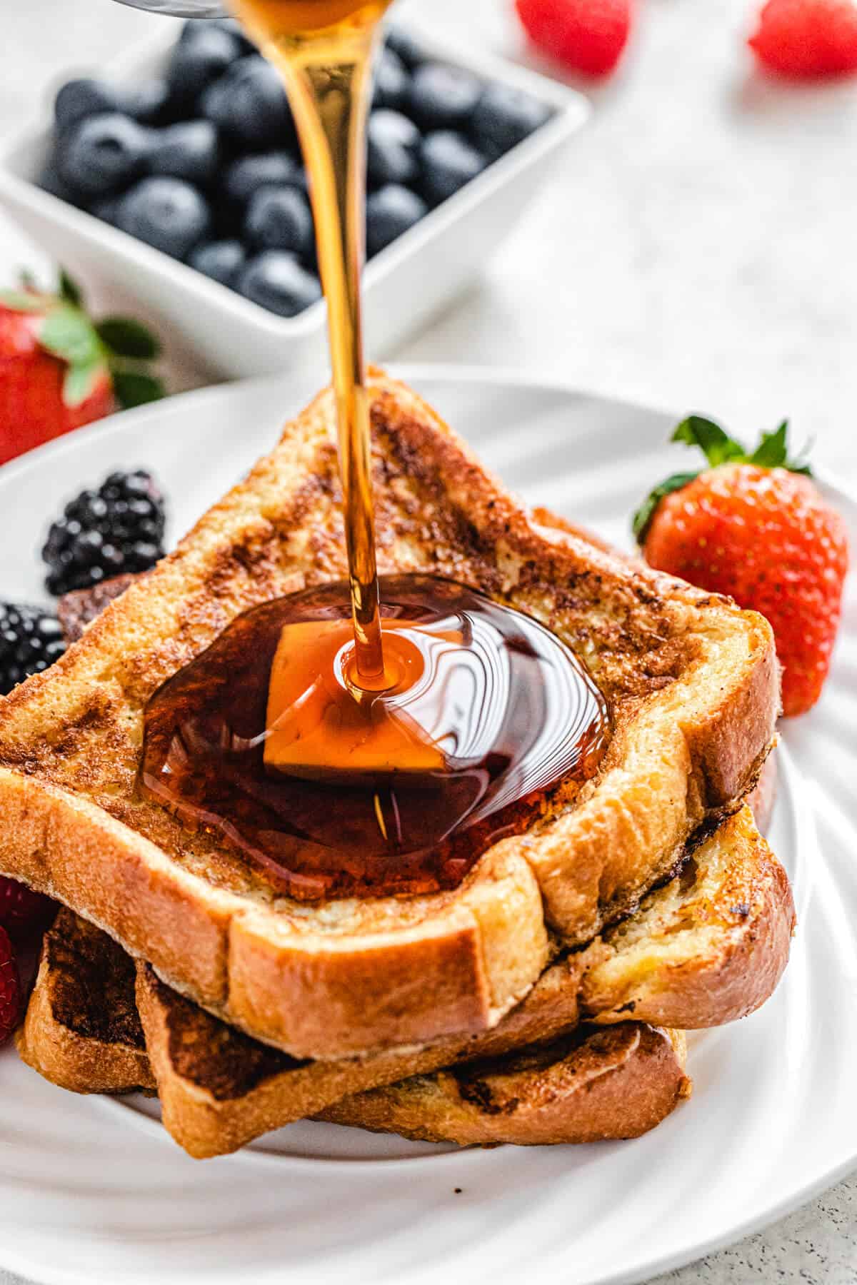 pouring maple syrup onto French toast on a white plate 