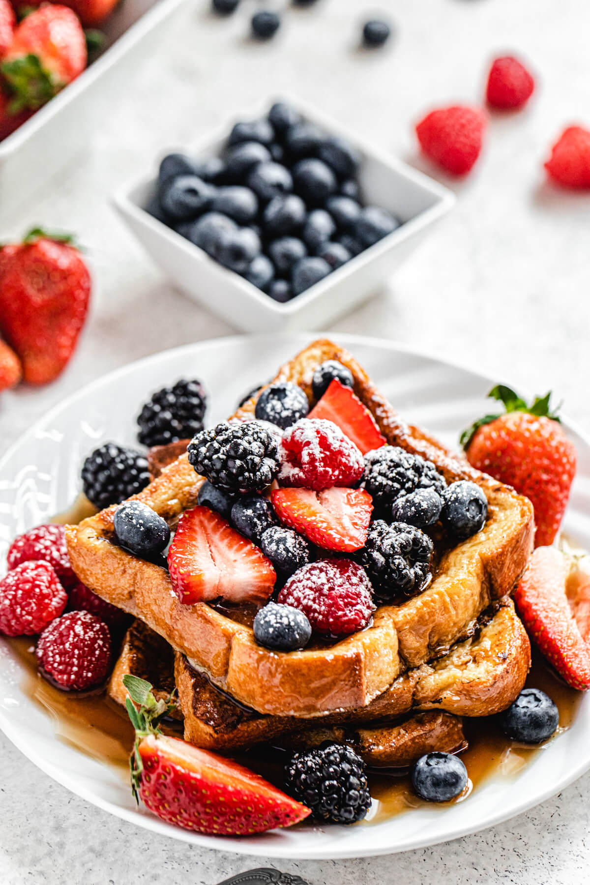 French toast on a white plate topped with fresh berries and powdered sugar