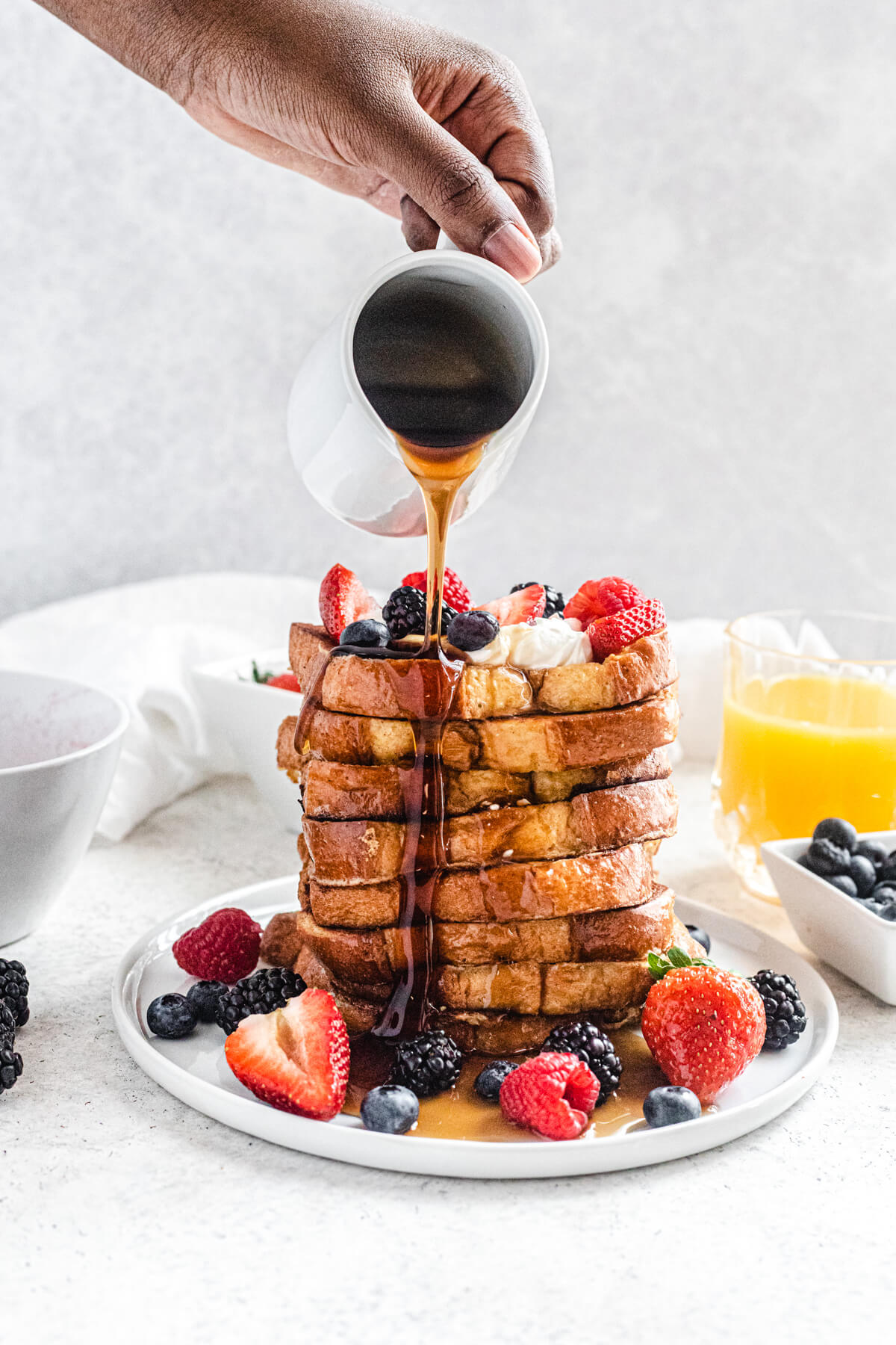 pouring maple syrup onto a tall stack of French toast topped with berries