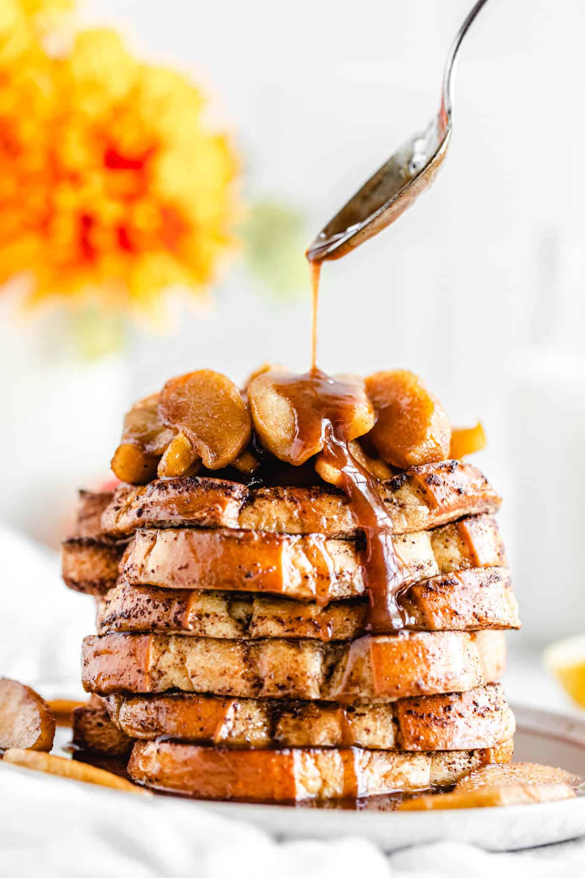 close up spooning syrup onto a stack of French toast on a plate