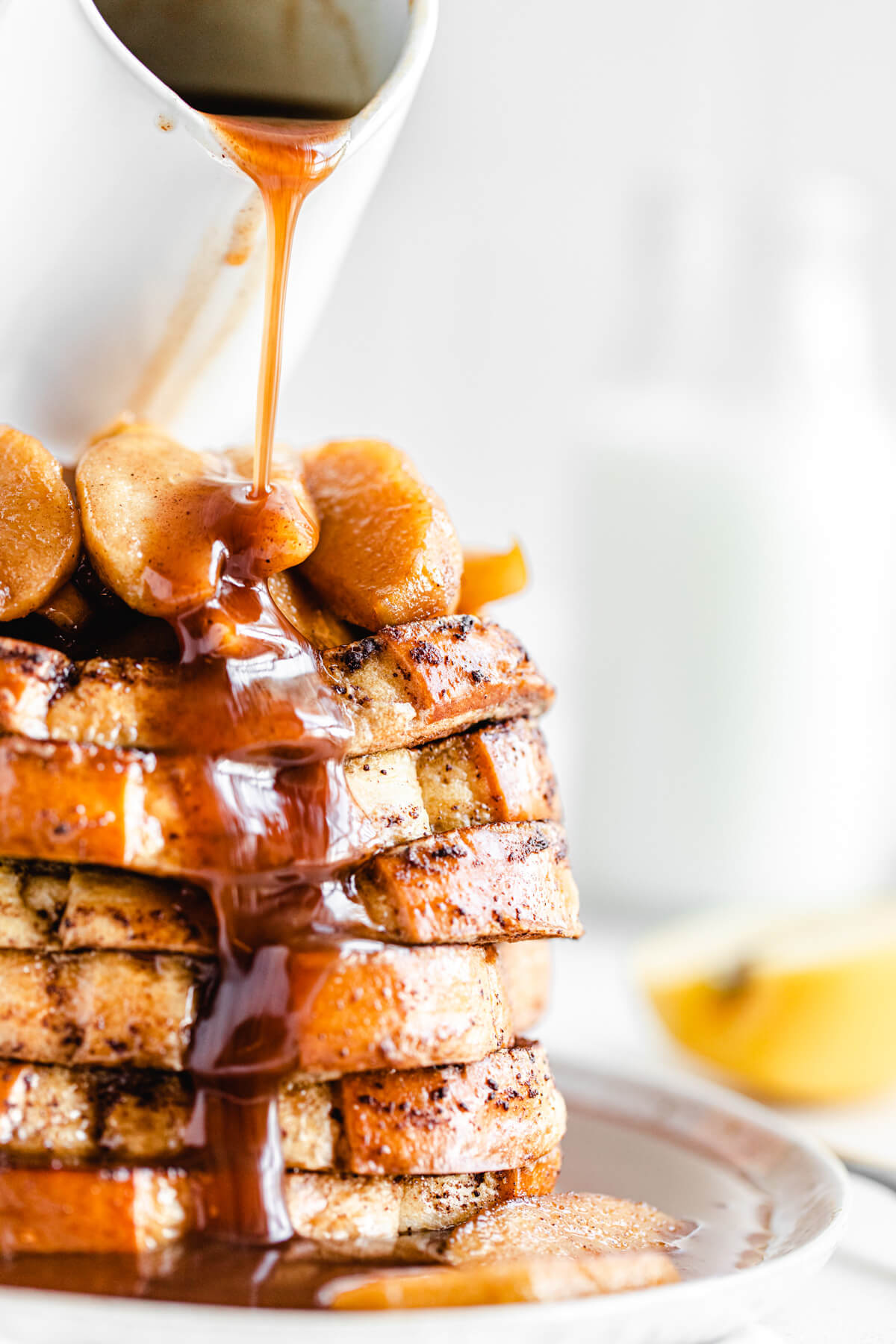 close up pouring syrup onto a stack of French toast topped with cooked apples