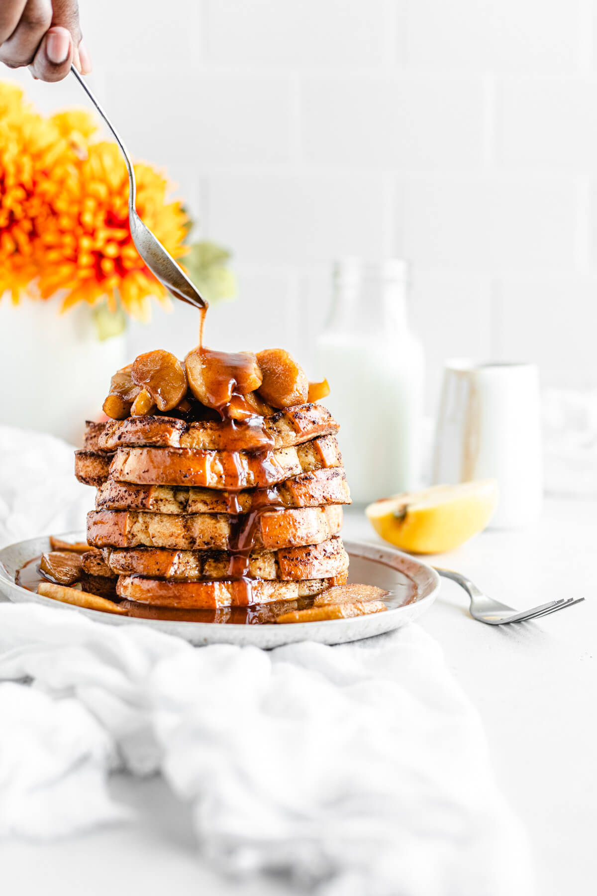 spooning syrup over a stack of French toast topped with apples