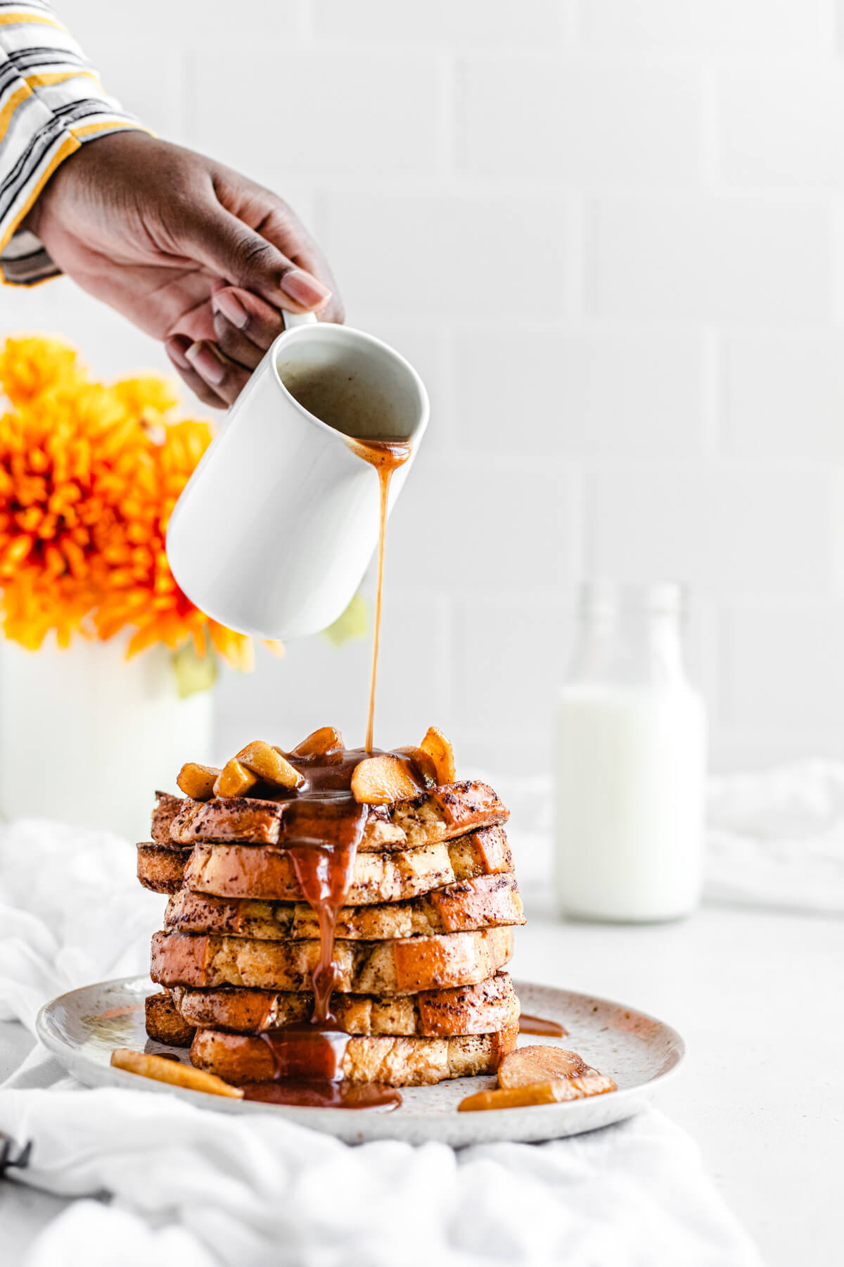 pouring syrup onto a stack of French toast topped with apples