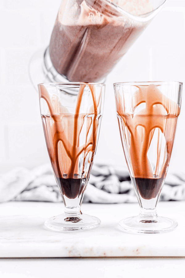 Gif of pouring milkshake into glasses and decorating with whipped cream, chocolate shavings, straws and a chocolate square