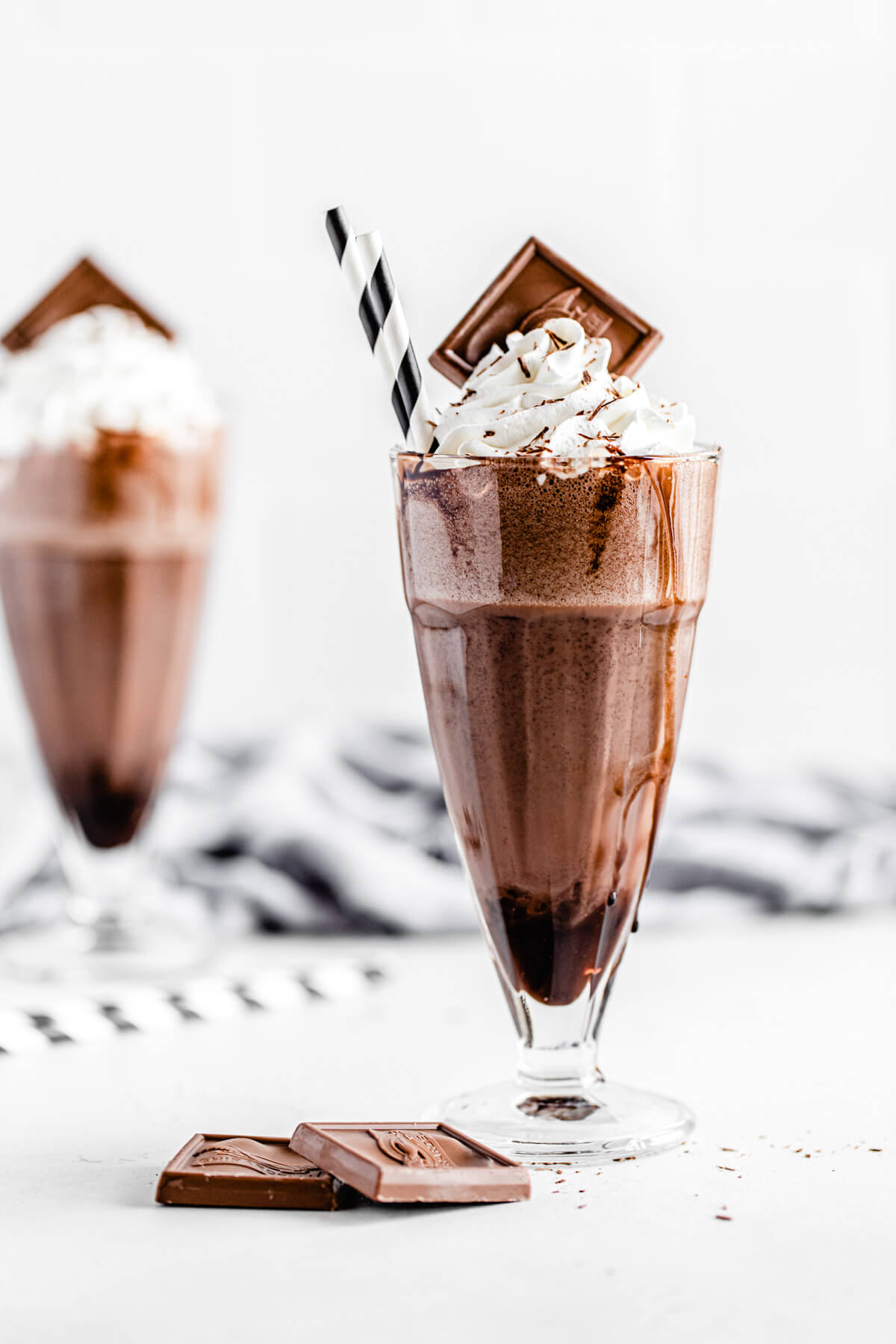 milkshake in the foreground with chocolate squares beside it and one milkshake in the background